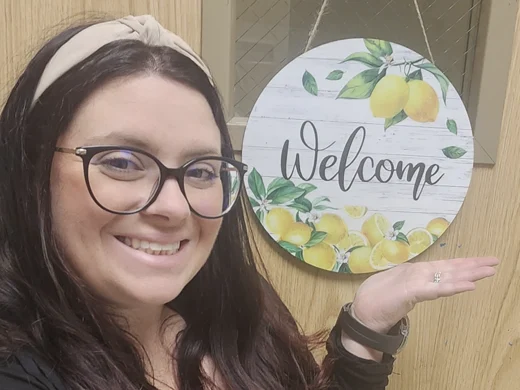 Miss Shay smiling beside a Welcome sign